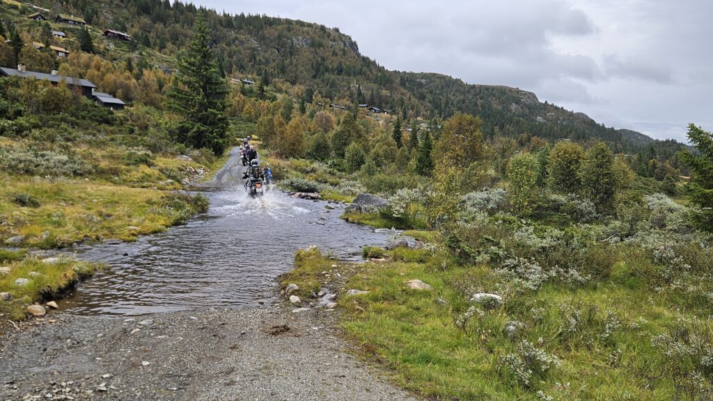 Motorsyklister krysser elv på grusvei under fjell adventure-kurs i Geilo med spektakulær natur i bakgrunnen./ Adventureskolen / Speed Motorcenter / Fjelltur MC / Motorsykkel