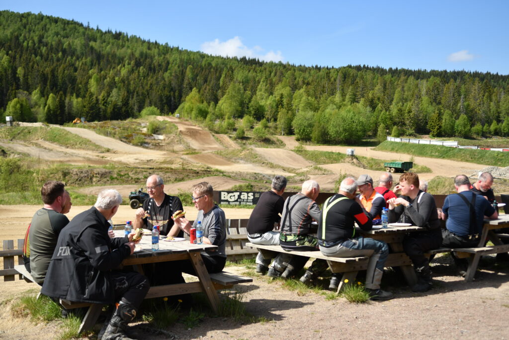 Utsikt mot treningsbanen mens deltakere nyter mat og drikke i solskinnet./ Adventureskolen / Speed Motorcenter / Kjørekurs MC / Motorsykkel