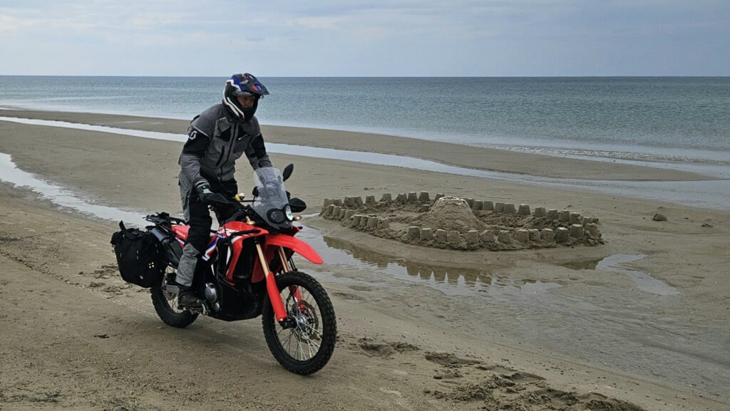 Kenny prøver CRF-en til Arkitekten på stranda – lettere og artigere i den løse sanda, med sandslott som bakteppe./ Speed Motorcenter / SpeedMC / Kyrre Hagen / MC-tur / MC-ferie / Motorsykkel / MC