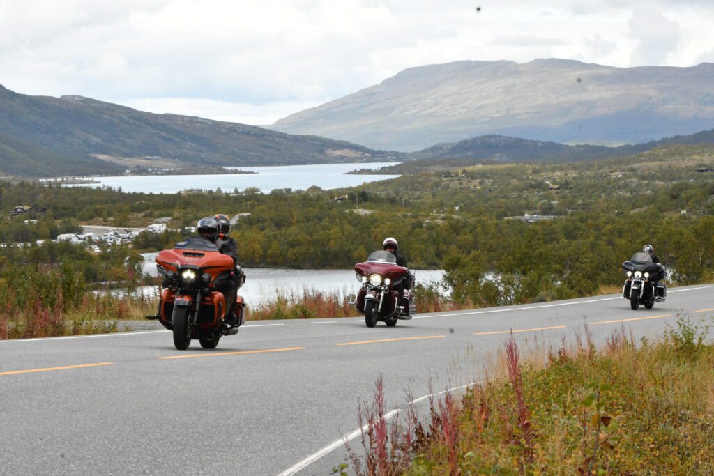 Tre touring-motorsykler på landeveien med fjell og vann i bakgrunnen. – Speed Motorcenter, Touringtreffet, Speed MC, Beitostølen, MC
